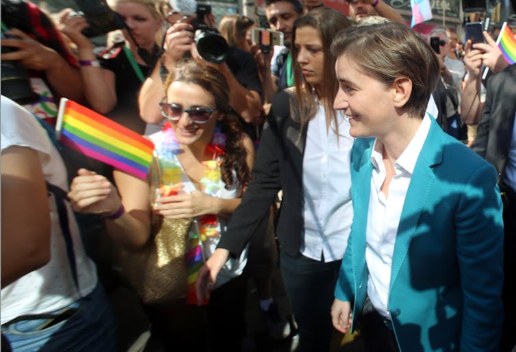 Serbian prime minister Ana Brnabic at the Belgrade Pride Parade in 2018 surrounded by people waving rainbow flags, balloons and banners.