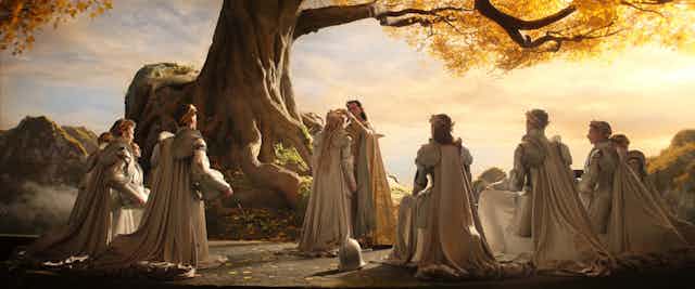 A group of elves kneel during a coronation by a tree.