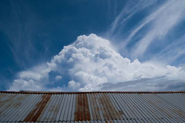 A cumulonimbus cloud towers above a corrugated iron roof.