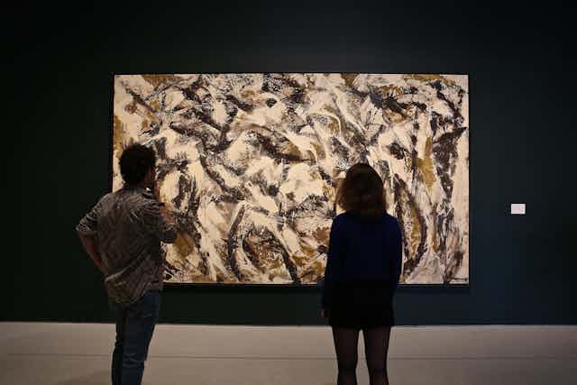 Two people standing in front of an abstract painting by Lee Krasner.