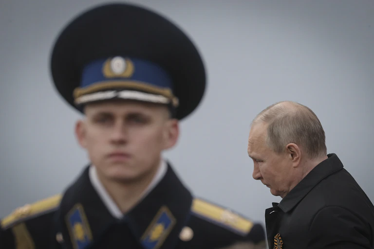 Vladimir Putin in an overcoat with a young military officer in the background.