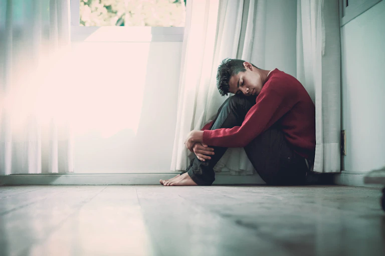 A young man sitting on the floor, with his head on his knees.