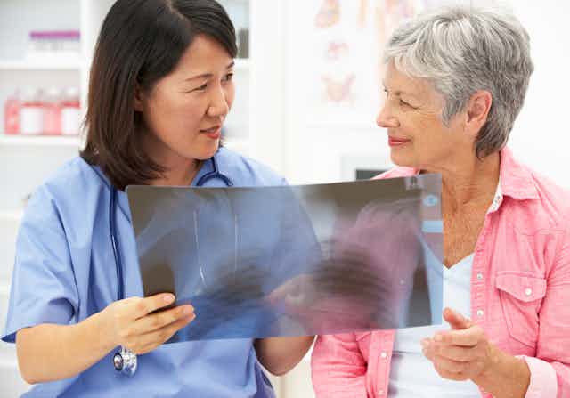 A woman in scrubs with a stethoscope around her neck showing an X-ray to an older woman in a pink shirt