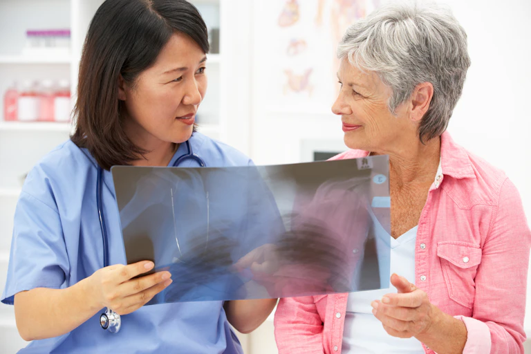 A woman in scrubs with a stethoscope around her neck showing an X-ray to an older woman in a pink shirt