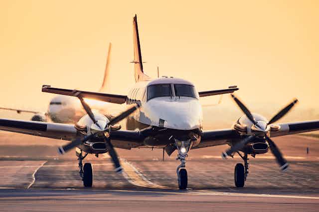 A turboprop plane and a larger jet on a runway at sunrise.