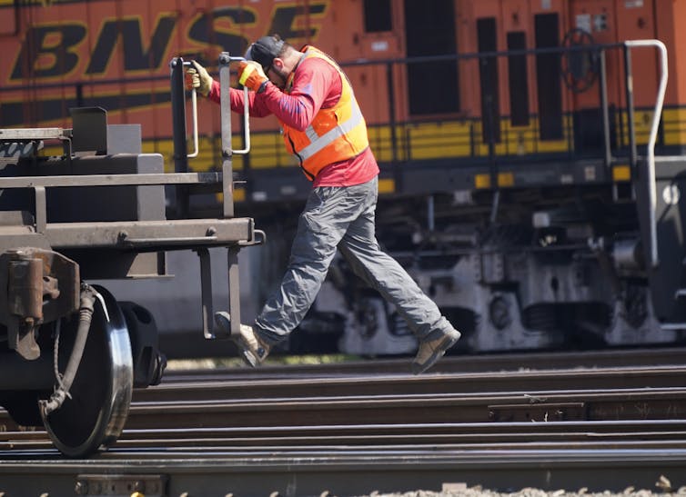 a rail worker wearing a safety vest rides a car on the tracks in front of bnsf logo on a train