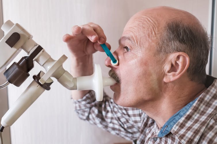 A man breathing into a white tube through his mouth, with a blue nose clip on his nose.