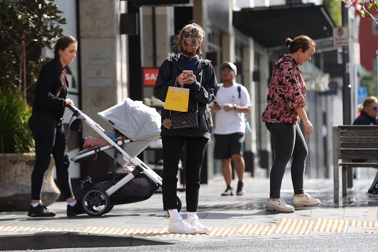 People walking in the street, with only one person wearing a mask, but not covering their nose.