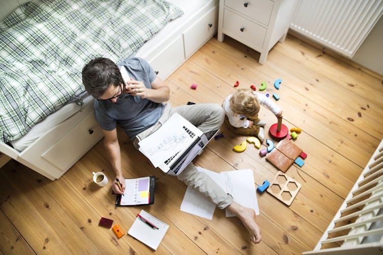 Man sitting on the floor working next to a child and surrounded by toys.