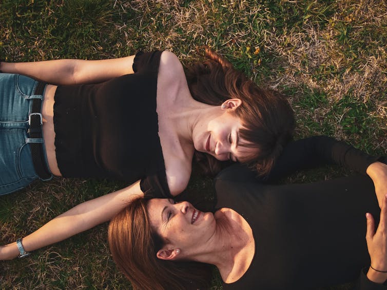 Mother and daughter lay on grass, looking at each other