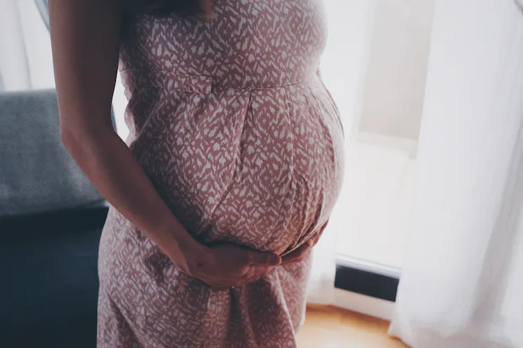 Pregnant woman holds her dress under her belly