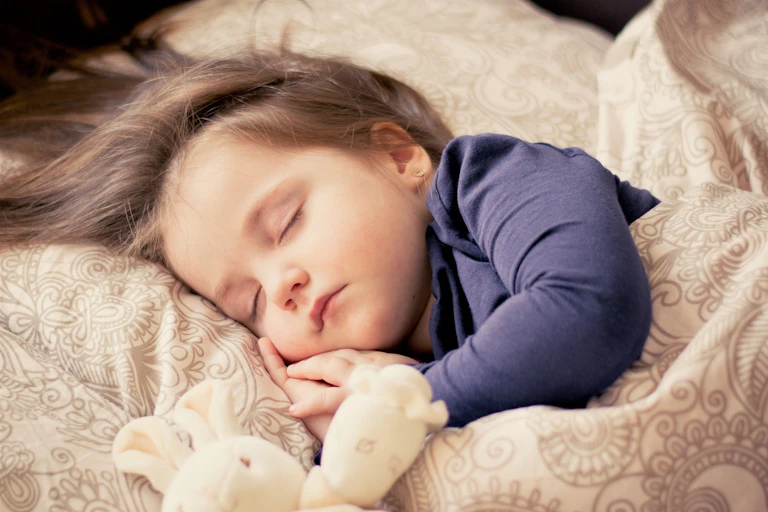 A girl sleeps with a toy in bed