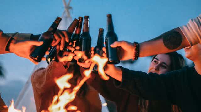 Young people clinking beer bottles around fire