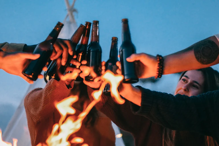 Young people clinking beer bottles around fire