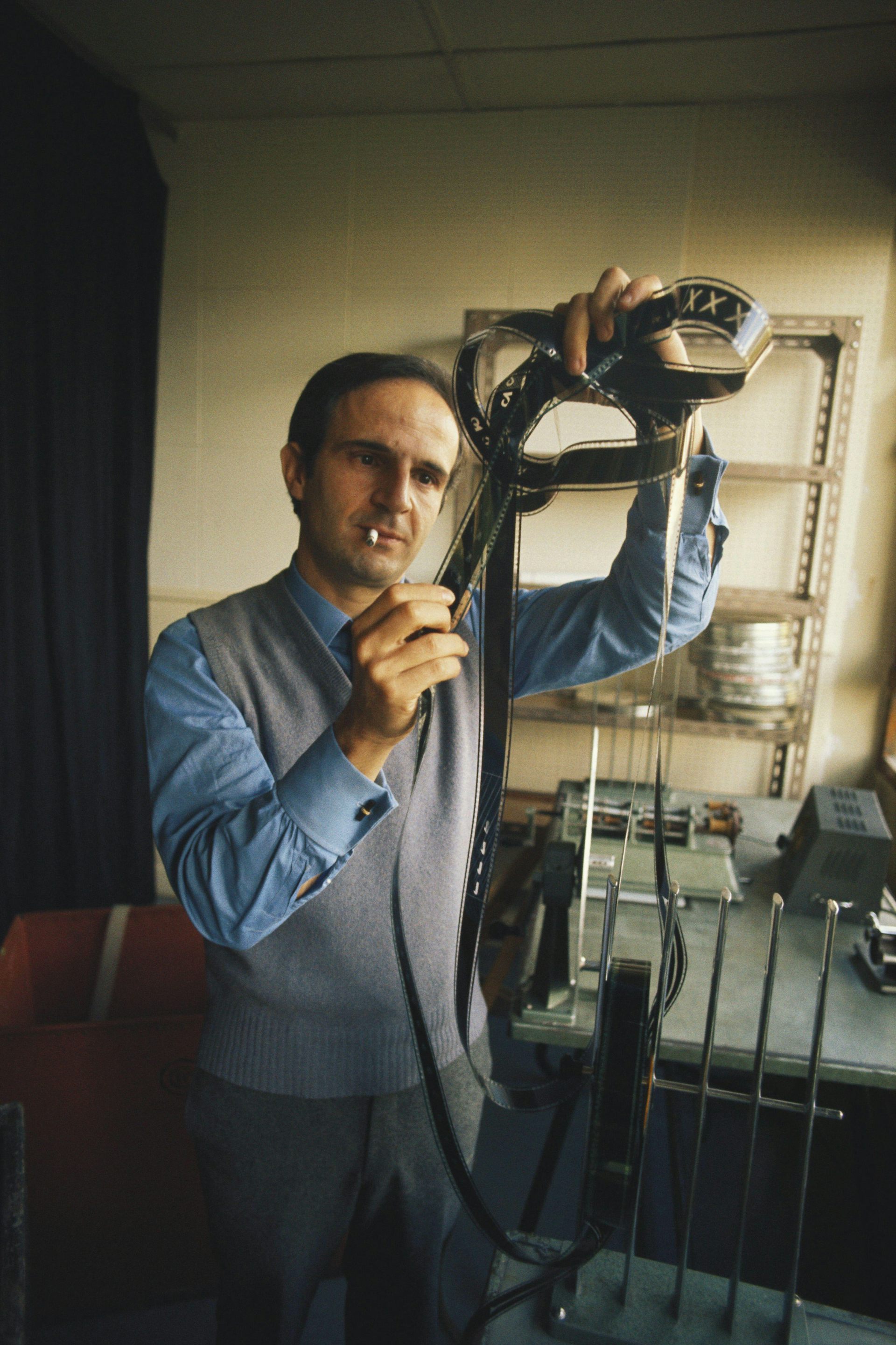 A man smoking a cigarette looking intently at some film reel negatives.
