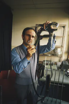 A man smoking a cigarette looking intently at some film reel negatives.