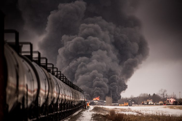 A huge cloud of smoke billows at the end of gleaming black rail cars.