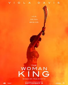 A movie poster with the words The Woman King and a woman in profile raising a sword against an orange and yellow backdrop.