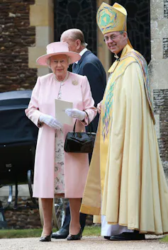 The Queen, wearing a pink jacket and hat, stands next to the Archbishop, wearing full regalia