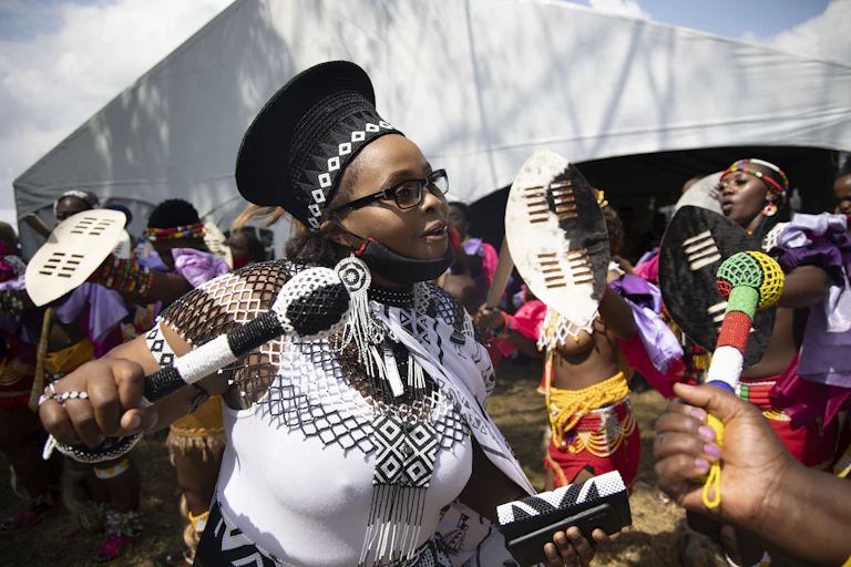 Women wearing colourful beadwork dance in front of a tent.
