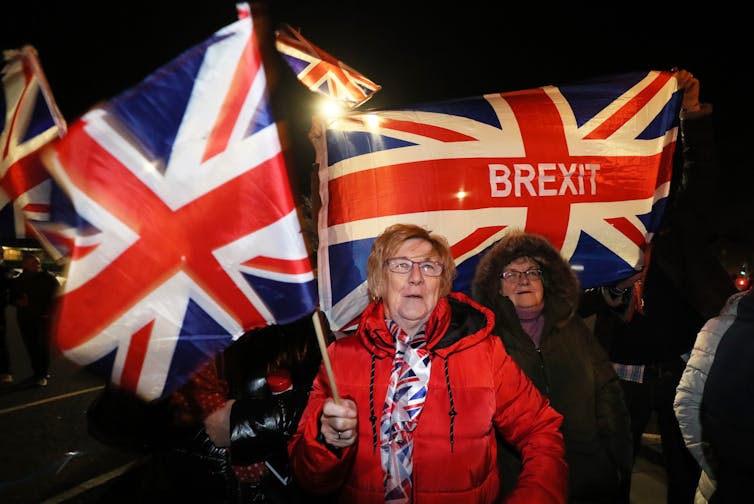 A woman in a red coat holds to British Union flags one with 'Brexit' written on it