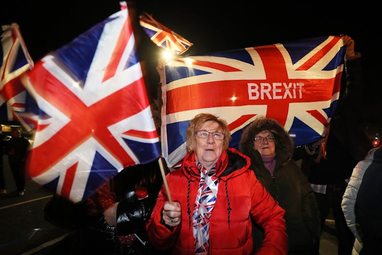 A woman in a red coat holds to British Union flags one with