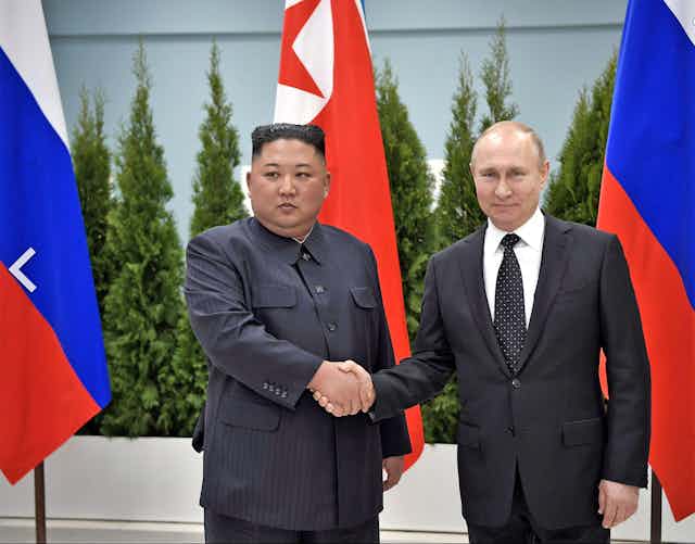 Two men shake hands in front of the Russian and North Korean flags.