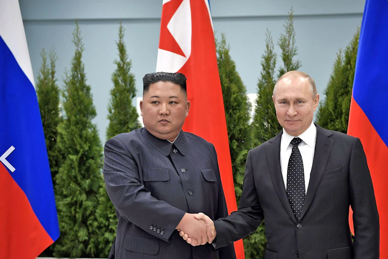 Two men shake hands in front of the Russian and North Korean flags.