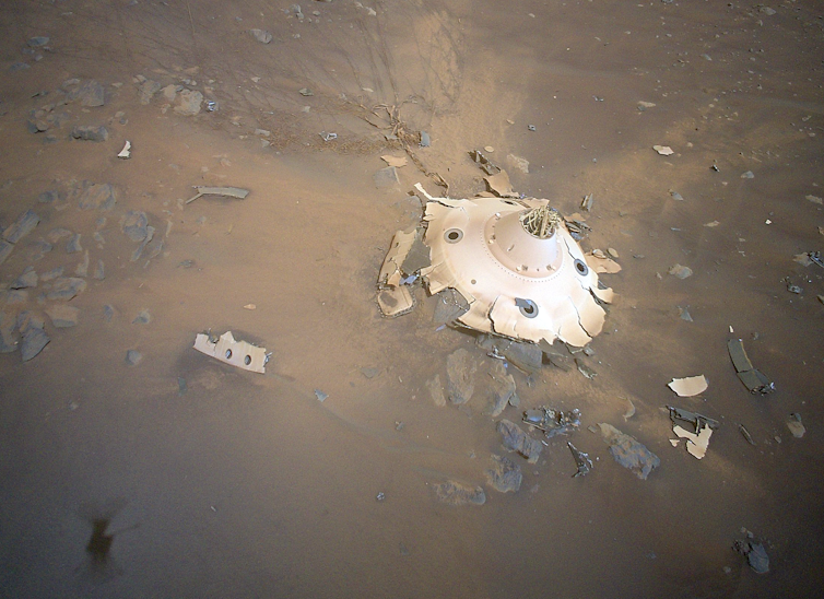 A smashed, round, white metal object on the surface of Mars.