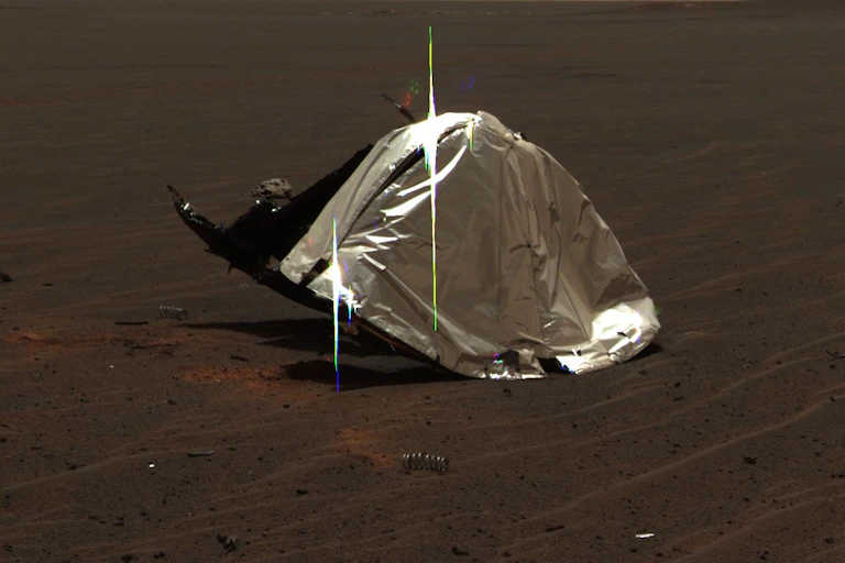 A shiny, silvery material with debris in the foreground on the surface of Mars.