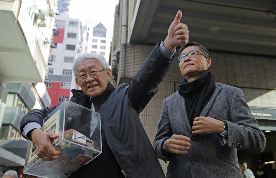Retired bishop of Hong Kong Cardinal Joseph Zen, left, holds a donation box, while another man stands by his side.