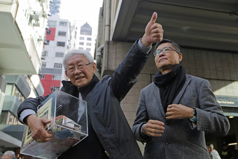 Retired bishop of Hong Kong Cardinal Joseph Zen, left, holds a donation box, while another man stands by his side.
