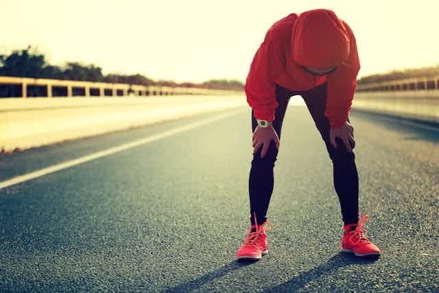 Une sportive appuie ses mains sur ses genoux pour récupérer après un effort intense