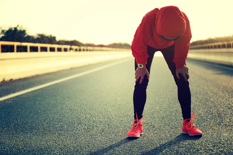 Une sportive appuie ses mains sur ses genoux pour récupérer après un effort intense