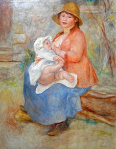A woman breastfeeds her child while sitting on a log.