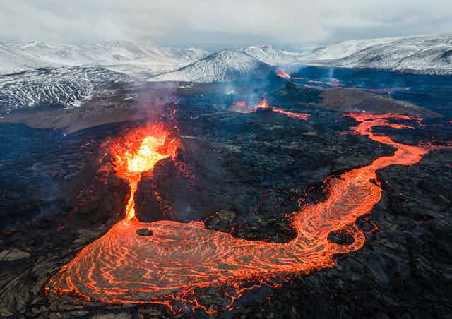 A river of bright orange lava flowing away from a bursting volcano