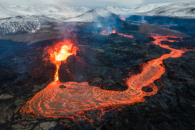 A river of bright orange lava flowing away from a bursting volcano