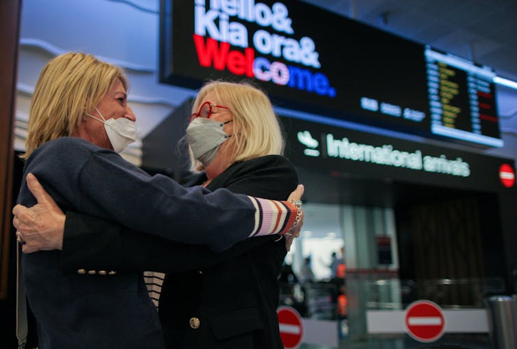 Two masked women hugging at the airport