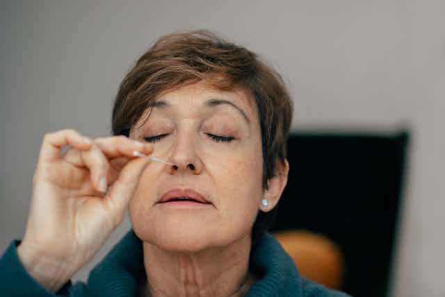 Older woman inserting nasal swab, yes shut