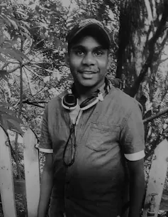 An Aboriginal person in black and white. They wear a hat and have headphones around their neck.