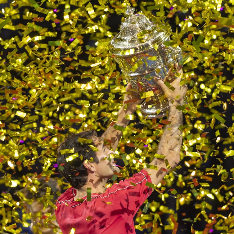 Federer holds a trophy, gold showers down.