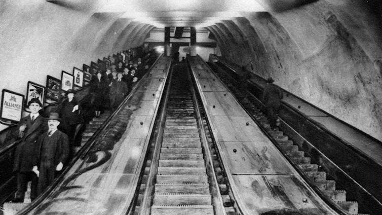 An archival photo of people on an escalator in an underground train station, in black and white.
