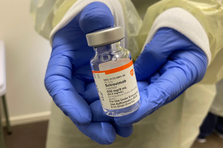 Gloved hands hold a vial of sotrovimab.