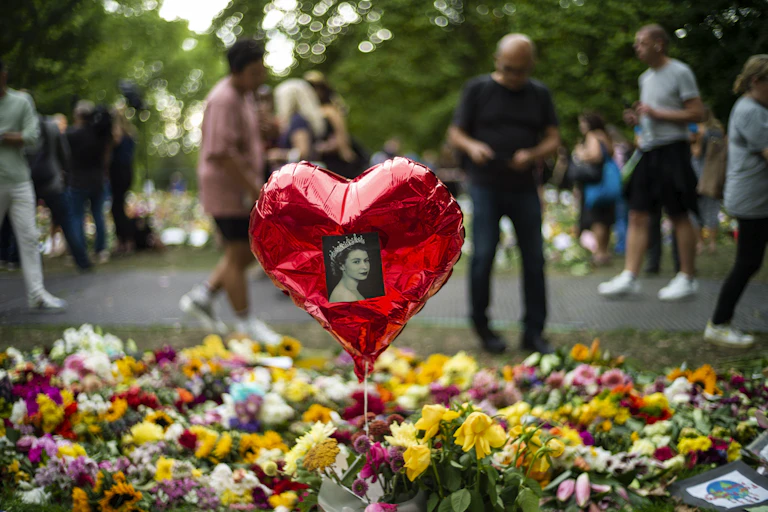 A balloon with a photo of the queen stuck on it floats above flowers left in her memory in London.