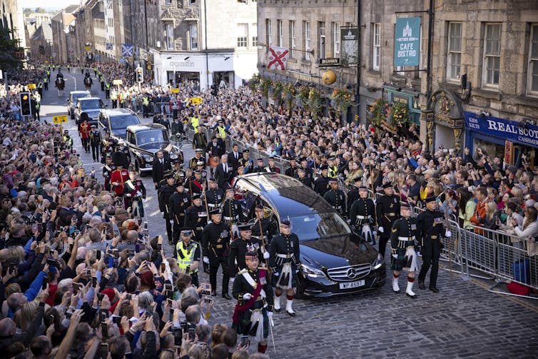 A hearse carrying the Queen's coffin driving through Edinburgh while crowds watch.