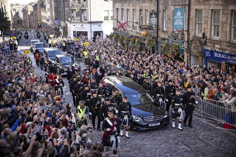 A hearse carrying the Queen's coffin driving through Edinburgh while crowds watch.