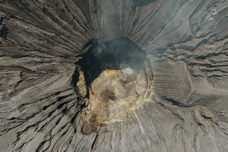 an overhead shot of a volcano crater with smoke