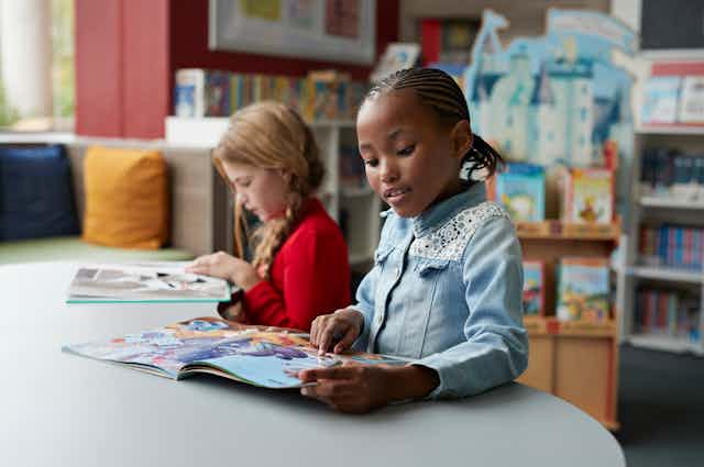 Two girls sit together at a table reading library books.
