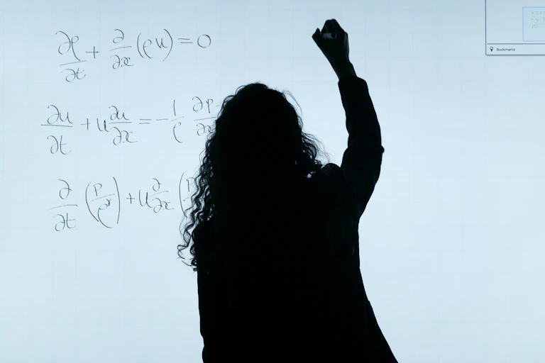A black silhouette of a woman writing equations on a whiteboard