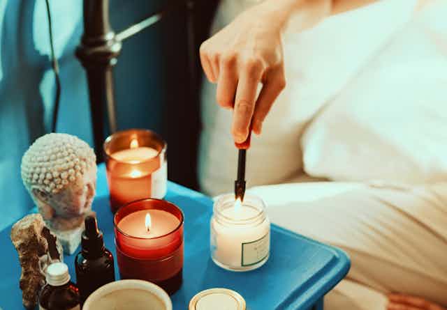 A person's hand lighting several scented candles on a blue bedside table